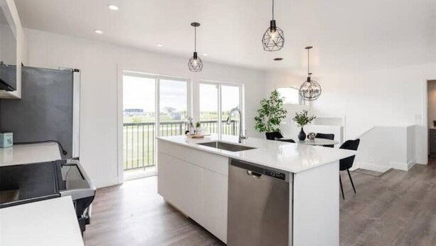 A modern kitchen with a central island, pendant lighting, and a view to the outside. - New waterfront- 5 bedroom home (Gimli)