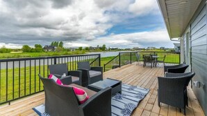 A covered outdoor deck with wicker furniture and a view of a lake. - New waterfront- 5 bedroom home (Gimli)