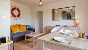 A modern living room with a sofa, a dining table with chairs, a small coffee table, a mirror, and a wall-mounted light fixture. - Le Surcouf by Interhome (Cabourg)