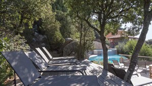 Una terraza de madera con sillones de descanso, una piscina y una vista de un edificio al fondo.