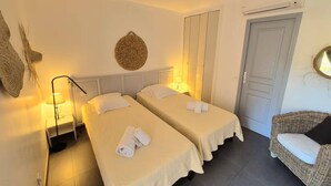 Una habitación de hotel con dos camas individuales, una silla de mimbre, una puerta y un adorno circular sujeto a la pared.