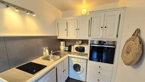 Una cocina compacta con armarios blancos, un microondas integrado, un lavamanos de acero inoxidable y una lavadora.