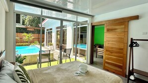 A bedroom with a large bed, a view of a swimming pool, and a sliding glass door leading to an outdoor area.