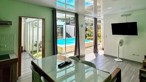 A modern kitchen with a large island, a dining area with chairs, and a view of a swimming pool through glass doors.