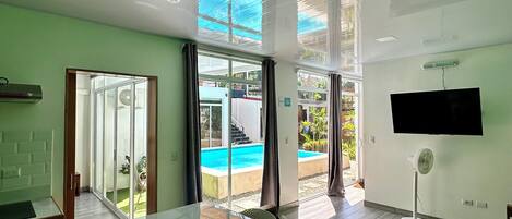 A modern kitchen with a large island, a dining area with chairs, and a view of a swimming pool through glass doors.
