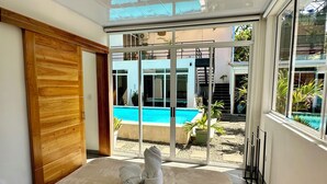 A modern bedroom with a large bed, a wooden wardrobe, and a view of a swimming pool through floor-to-ceiling glass doors.