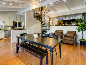 A spacious living area with a dark wooden dining table, a built-in bench, and a spiral staircase.