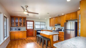 A kitchen with wooden cabinets, a stainless steel refrigerator, a microwave, and a ceiling fan. - Serene Riverfront Home · Hot Tub + Private River Access – Just 150 Yards Away (Three Rivers)