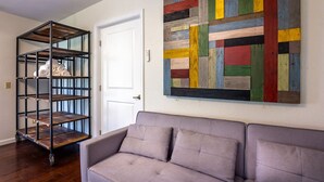 A room with a grey sofa, a metal shelving unit with towels, and a colorful abstract painting on the wall. - Serene Riverfront Home · Hot Tub + Private River Access – Just 150 Yards Away (Three Rivers)