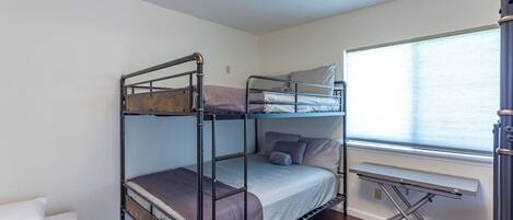 Een slaapkamer met stapelbed, bureau en raam.