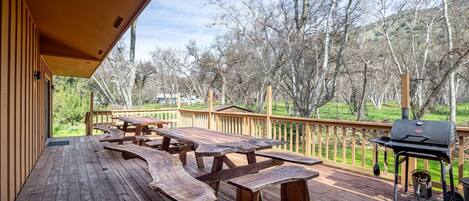 A wooden deck with picnic tables and a grill.