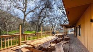 An outdoor deck with picnic tables, a barbecue grill, and a view of a wooded area. - Serene Riverfront Home · Hot Tub + Private River Access – Just 150 Yards Away (Three Rivers)