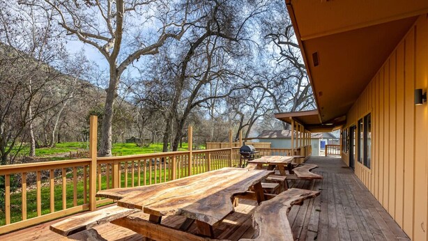 An outdoor deck with picnic tables, a barbecue grill, and a view of a wooded area. - Serene Riverfront Home · Hot Tub + Private River Access – Just 150 Yards Away (Three Rivers)