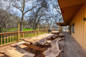 Una terraza al aire libre con mesas de picnic, una parrilla y vistas a un área boscosa.