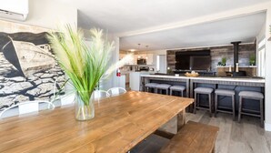 Cozinha moderna com ilha central, banquetas e mesa de jantar de madeira.