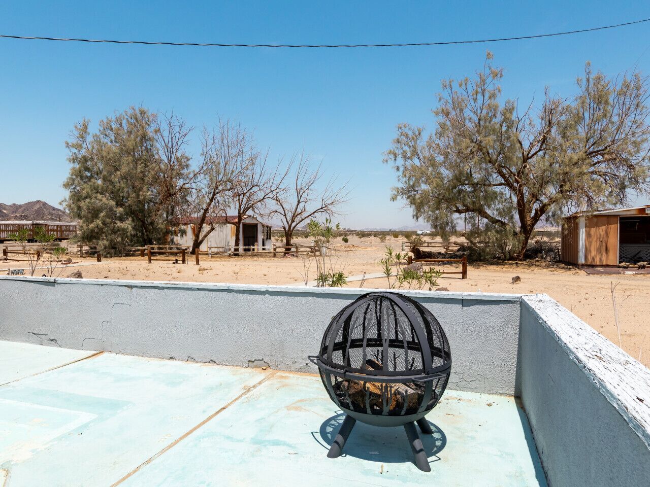 A rooftop with a metal cage structure, a clear blue sky, and sparse vegetation in the background.