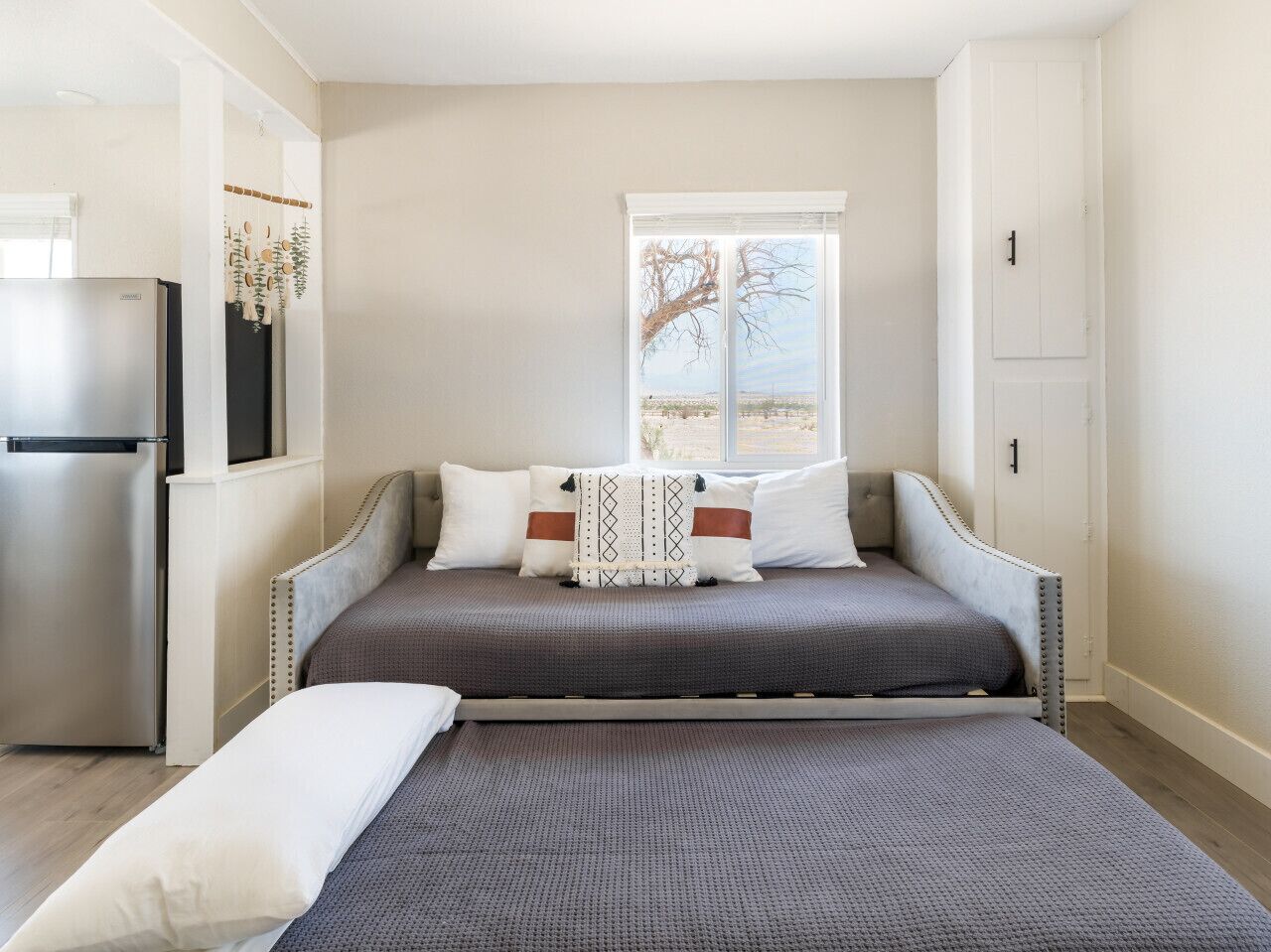 Un dormitorio con cama, ventana y refrigerador.