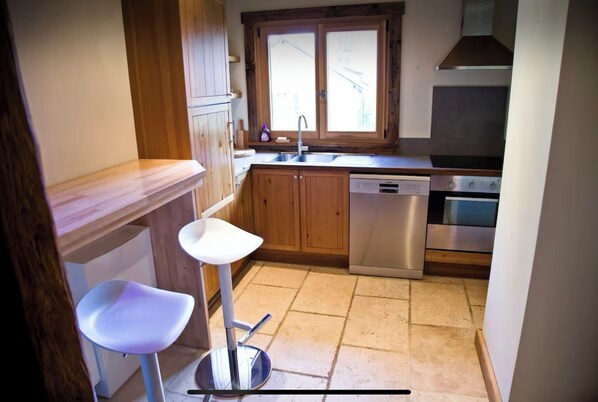 A compact kitchen with wooden cabinets, a stainless steel dishwasher, and a double oven.