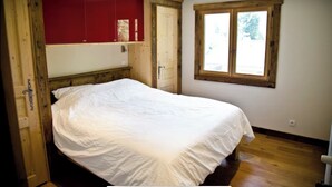 Un dormitorio con estructura de cama de madera, un armario rojo y una ventana con vistas a árboles.