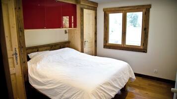 Une chambre à coucher avec un lit en bois, une armoire rouge et une fenêtre donnant sur les arbres.