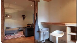 Una habitación acogedora con techo de madera, un sofá, una mesa de comedor con sillas y un lavamanos pequeño.