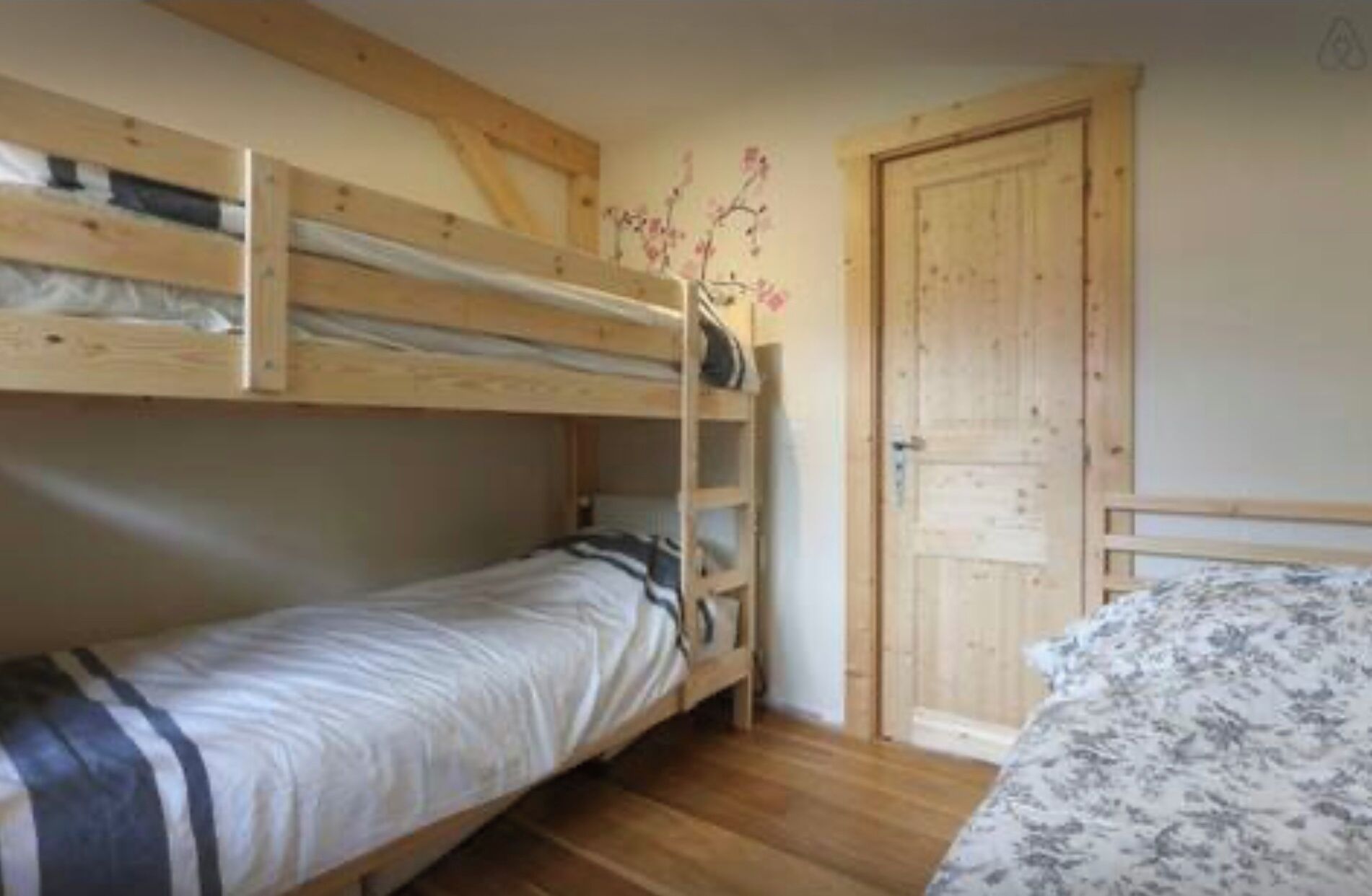 A room with two bunk beds, a wooden ladder, a door, and a patterned bedspread.