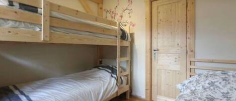A room with two bunk beds, a wooden ladder, a door, and a patterned bedspread.