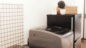 A compact kitchen with a built-in washer and dryer, a small countertop, and a decorative plant. - Cozy Studio Apartment (Ho Chi Minh City)