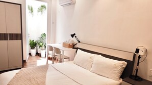 A bedroom with a bed, bedside table, lamp, and a desk with chairs. - Cozy Studio Apartment (Ho Chi Minh City)