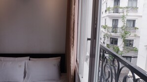 A hotel room with a bed, a window with a view of a building with balconies. - Cozy Studio Apartment (Ho Chi Minh City)