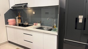 Una cocina moderna con armarios blancos, un refrigerador negro, un lavabo con escurreplatos y una cocedora de arroz rosa.