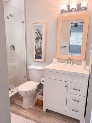 A bathroom with a toilet, sink, cabinet, and shower.