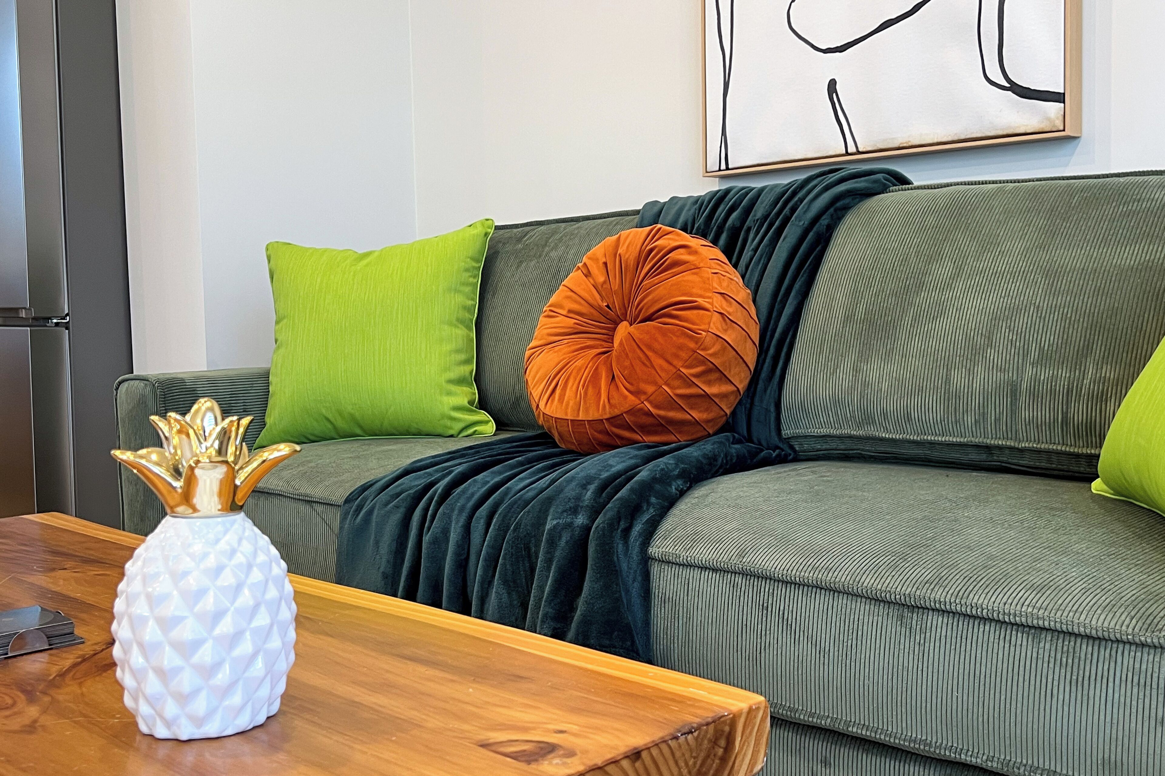 Un salon moderne avec un canapé vert, un vase en forme d’ananas et une table basse en bois.