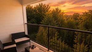A balcony with wicker furniture, a patterned rug, and a view of trees at sunset. - Austin 3BR Home for Families & Groups · Sleeps 10 · 10min to UT (Austin)