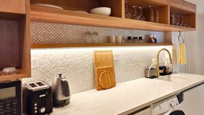A kitchen with wooden shelves, a countertop, a kettle, a toaster, a sink, and a washing machine. - Tui Studio | New Reno| Self Contained | Near City (Auckland)