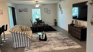 A modern living room with a striped sofa, a glass coffee table, and a TV mounted on the wall. - Spacious 5-bedroom house in welcoming Sebastian with WiFi, AC (Vero Beach)