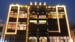 A building with large windows and a central archway, illuminated by string lights. - BUSAN ALMOND KIDS POOL VILLA NAMPO (Busan)