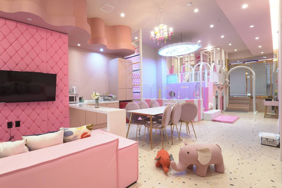 A modern interior with a pink color scheme, including a seating area, dining space, and a play area with a slide.
