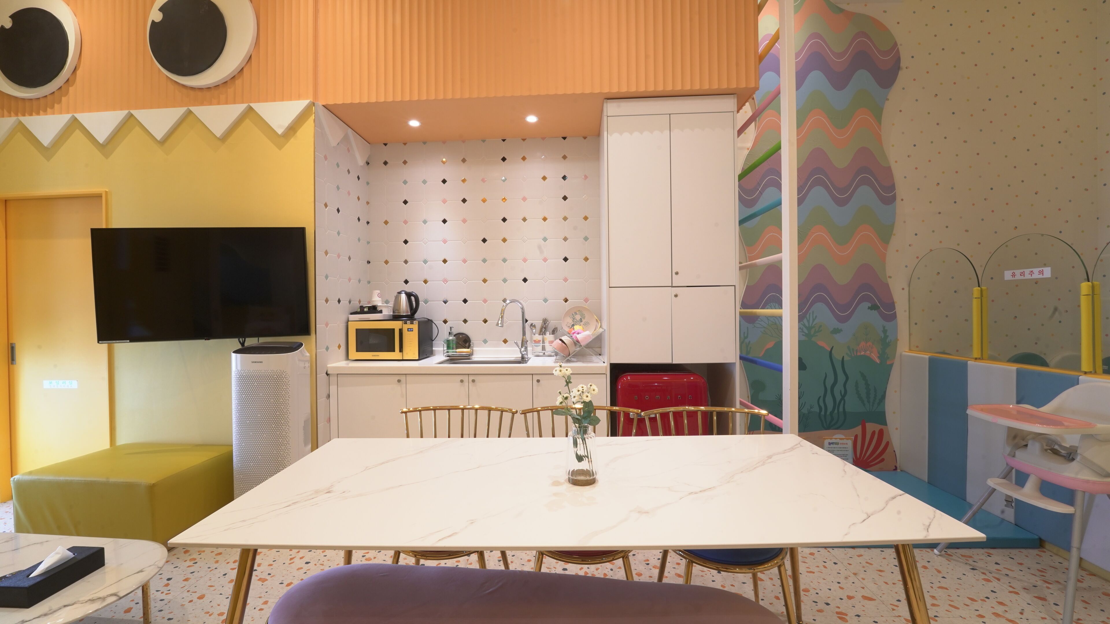 Una cocina funcional con microondas, pileta y pequeño refrigerador. Hay una mesa de comedor con sillas y un florero con flores.