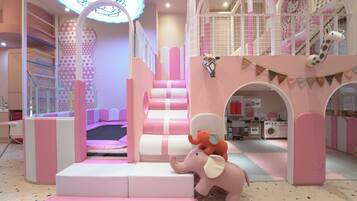 A children's play area with a pink and white color scheme, including a slide, a playhouse, and a toy kitchen.