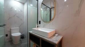 A modern bathroom with a white toilet, a rectangular sink with a marble countertop, and a round mirror with a gold frame.