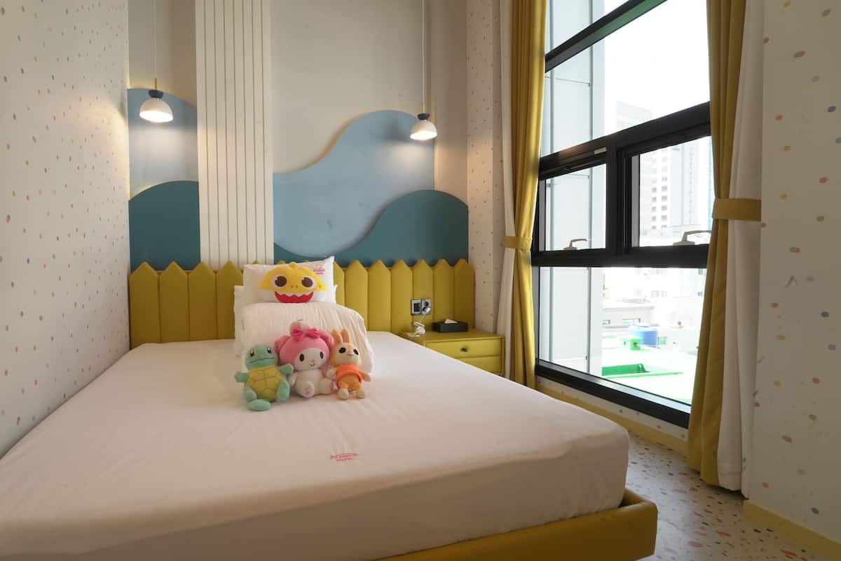 A bed with a white mattress, a yellow headboard, and a window with a view of buildings.