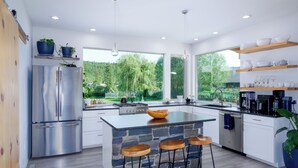 Une cuisine moderne dotée d’un grand îlot central, d’appareils électroménagers en acier inoxydable et offrant une vue sur l’extérieur.