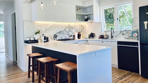 Een moderne keuken met een marmeren achterwand, een centraal eiland met krukken en een vaatwasser.