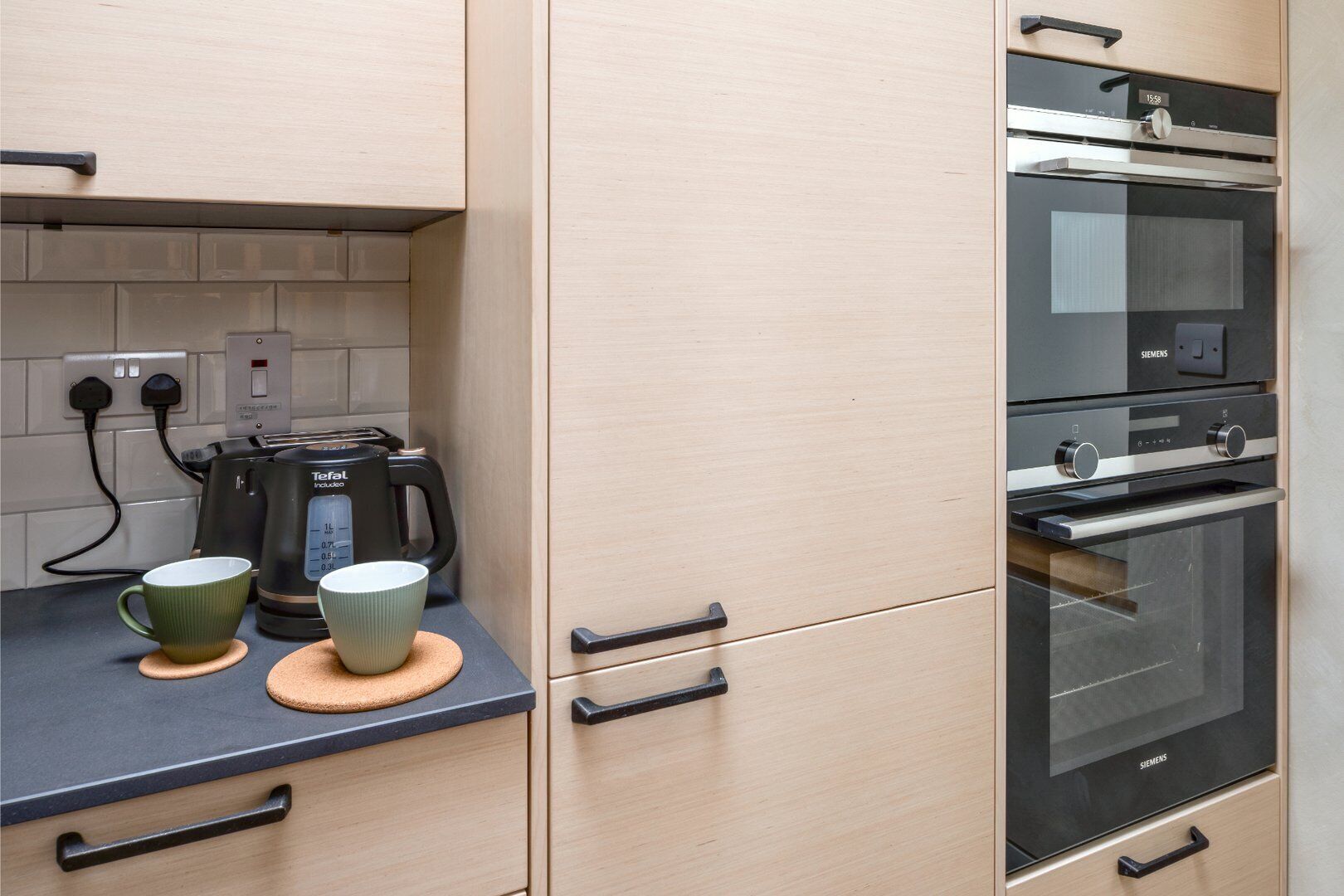 Una cocina con horno Siemens, una cafetera y dos tazas sobre la encimera.