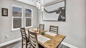 Un coin repas avec une table en bois, quatre chaises, un lustre et des œuvres d’art accrochées au mur.