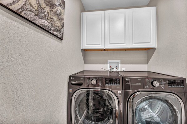 A laundry area with a front-loading washer and dryer, white cabinets above, and a marble artwork on the wall.