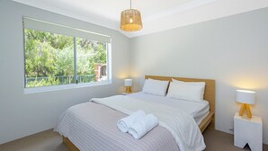 Un dormitorio con un ventanal grande, una cama con ropa de cama blanca, dos lámparas de noche y un aplique.