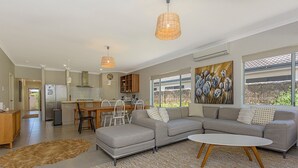 Una sala de estar moderna con un sofá seccional gris, un comedor con mesa y sillas de madera, y una cocina con estufa empotrada y armarios blancos.
