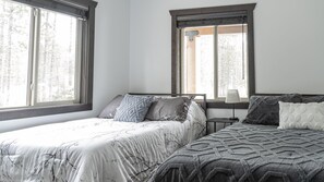 Une chambre avec deux lits, de grandes fenêtres et une table de chevet avec une lampe.